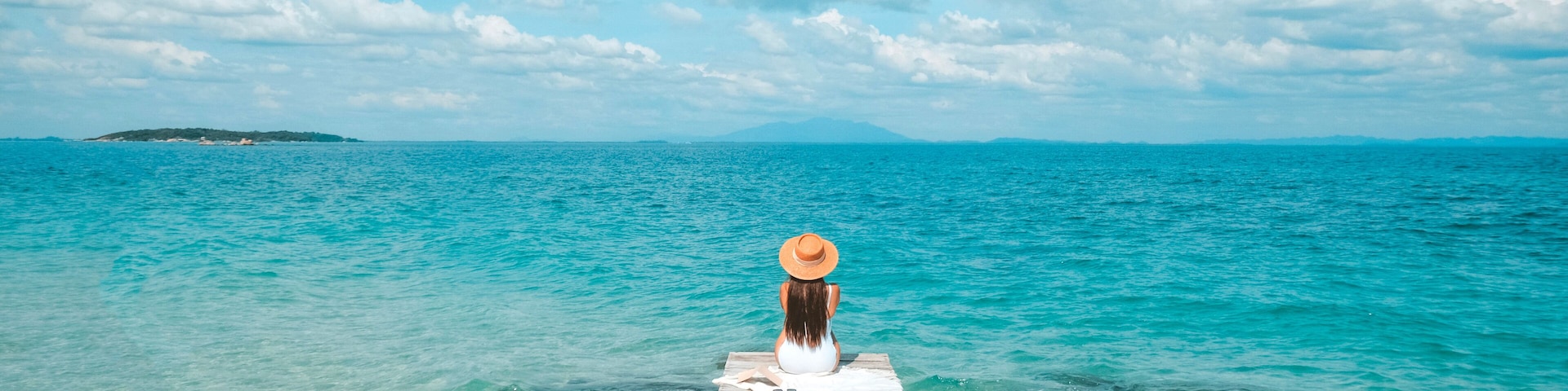 Alone woman sitting by the sea enjoying the blue ocean view at the beach. Travel pictures and vacation at Kho Mun Nork, Thailand.