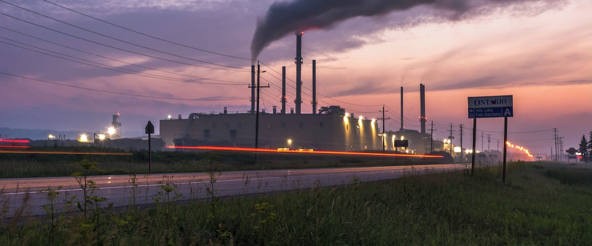 A power plant with smoke stacks, a road with light trails, and a sign for Ontario.