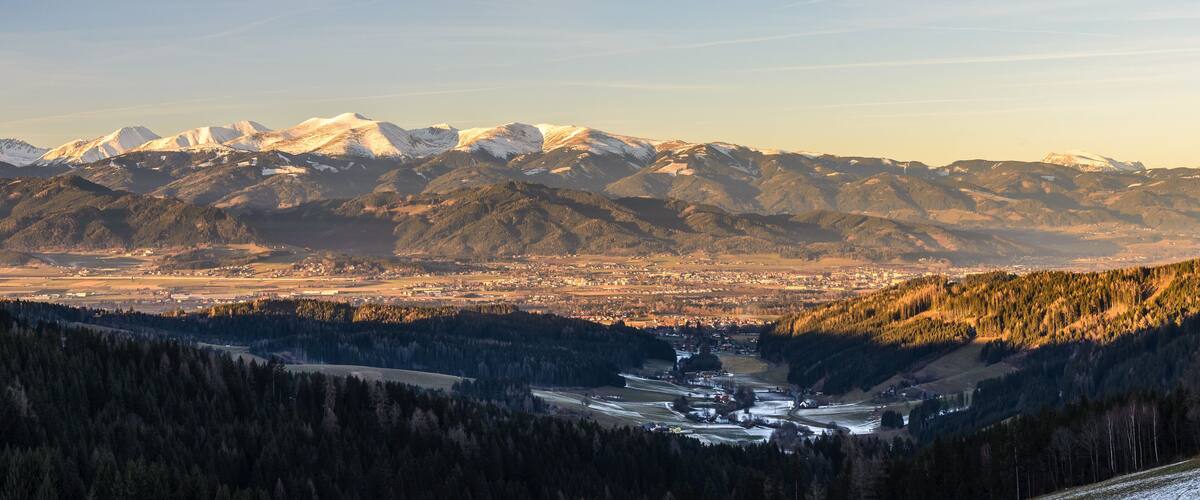 A mountainous landscape with snow-capped peaks, a valley with a river, and a town in the distance.