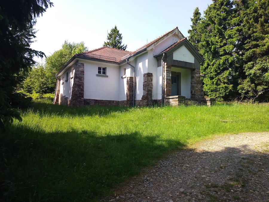 Ein kleines Steinhaus mit rotem Dach, umgeben von üppiger Vegetation.