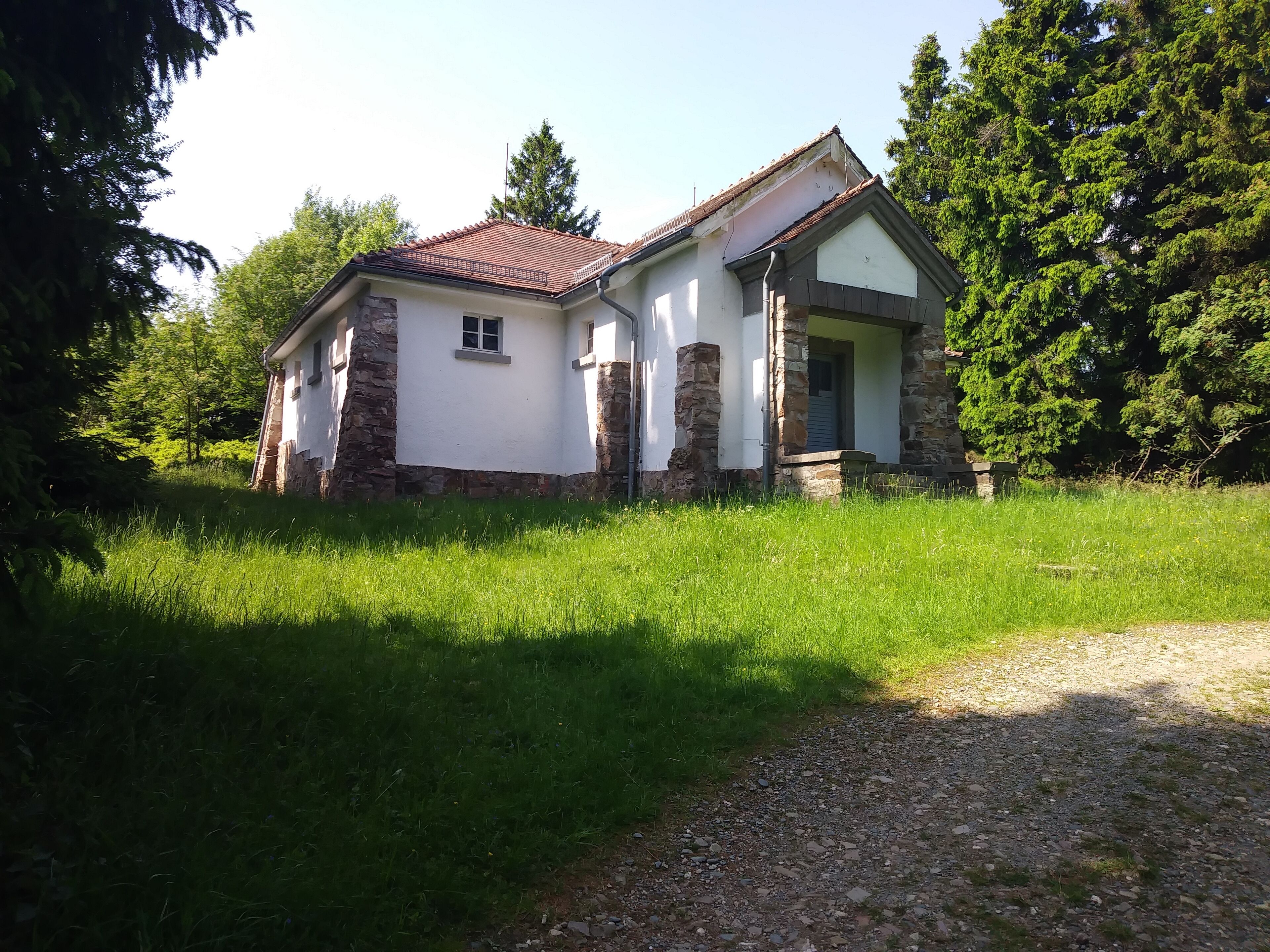 A small stone house with a red roof surrounded by lush greenery.