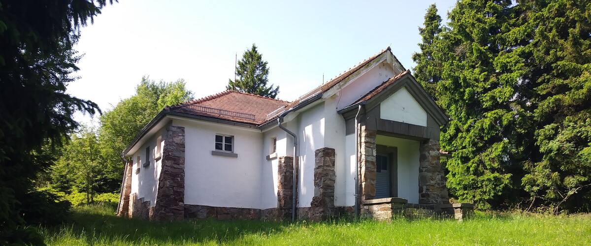 A small stone house with a red roof surrounded by lush greenery.
