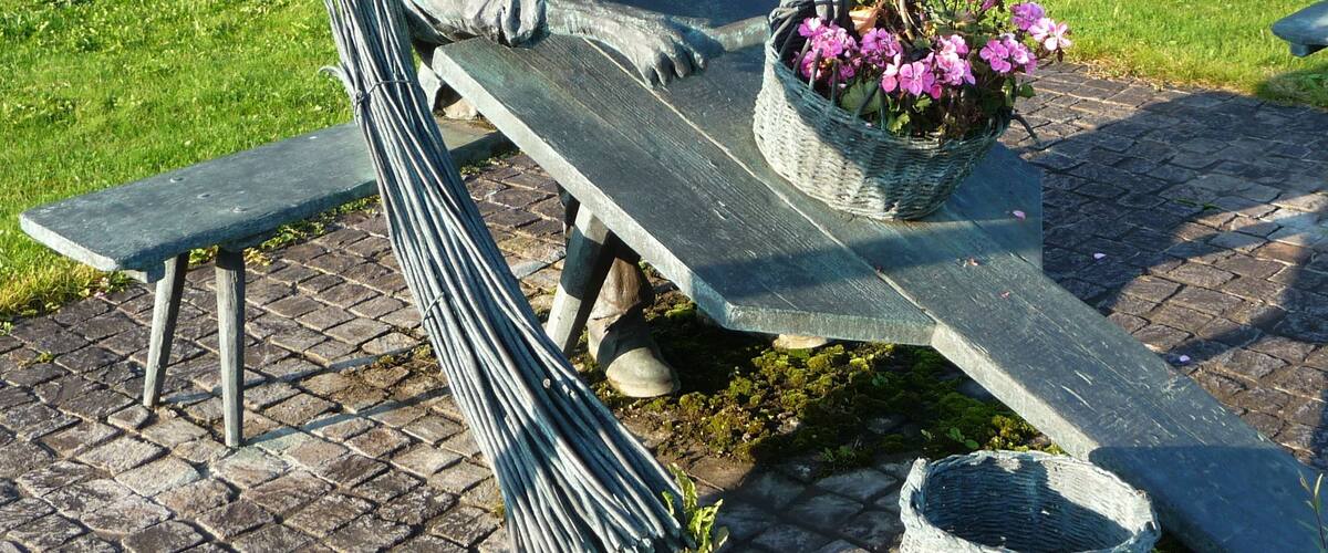 A statue of a man sitting on a bench with a basket of flowers.