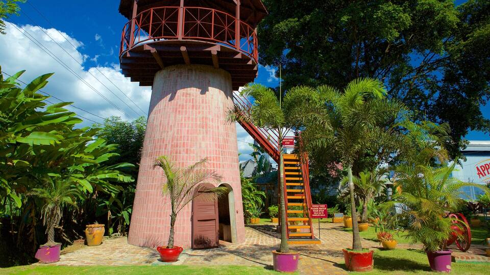 A brick lighthouse with a red balcony, surrounded by tropical plants and a viewing tower.