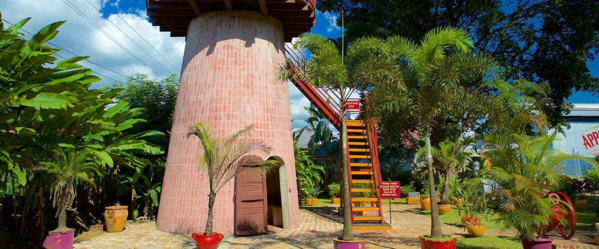 A brick lighthouse with a red balcony, surrounded by tropical plants and a viewing tower.