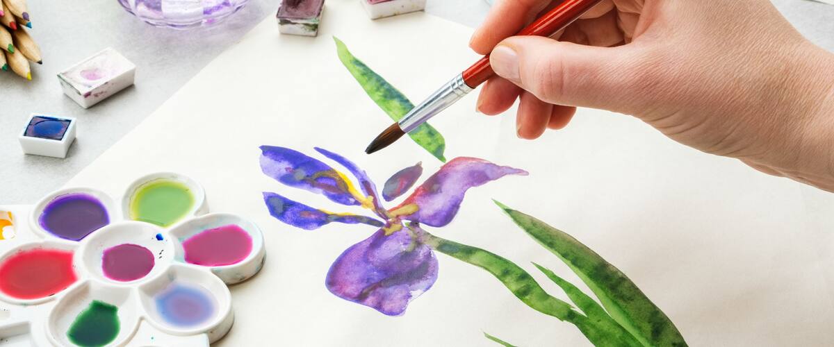 Iris flower and artistic equipment on desk. Top view. Painter drawing at working place.