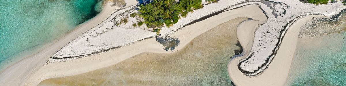 An aerial view of a beach with a curved sandbar, clear turquoise waters, and a small island.