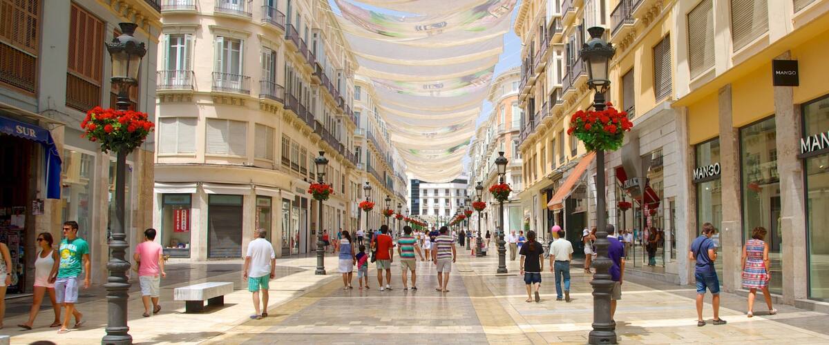 A pedestrian street lined with multi-story buildings, featuring balconies, flower baskets, and storefronts.