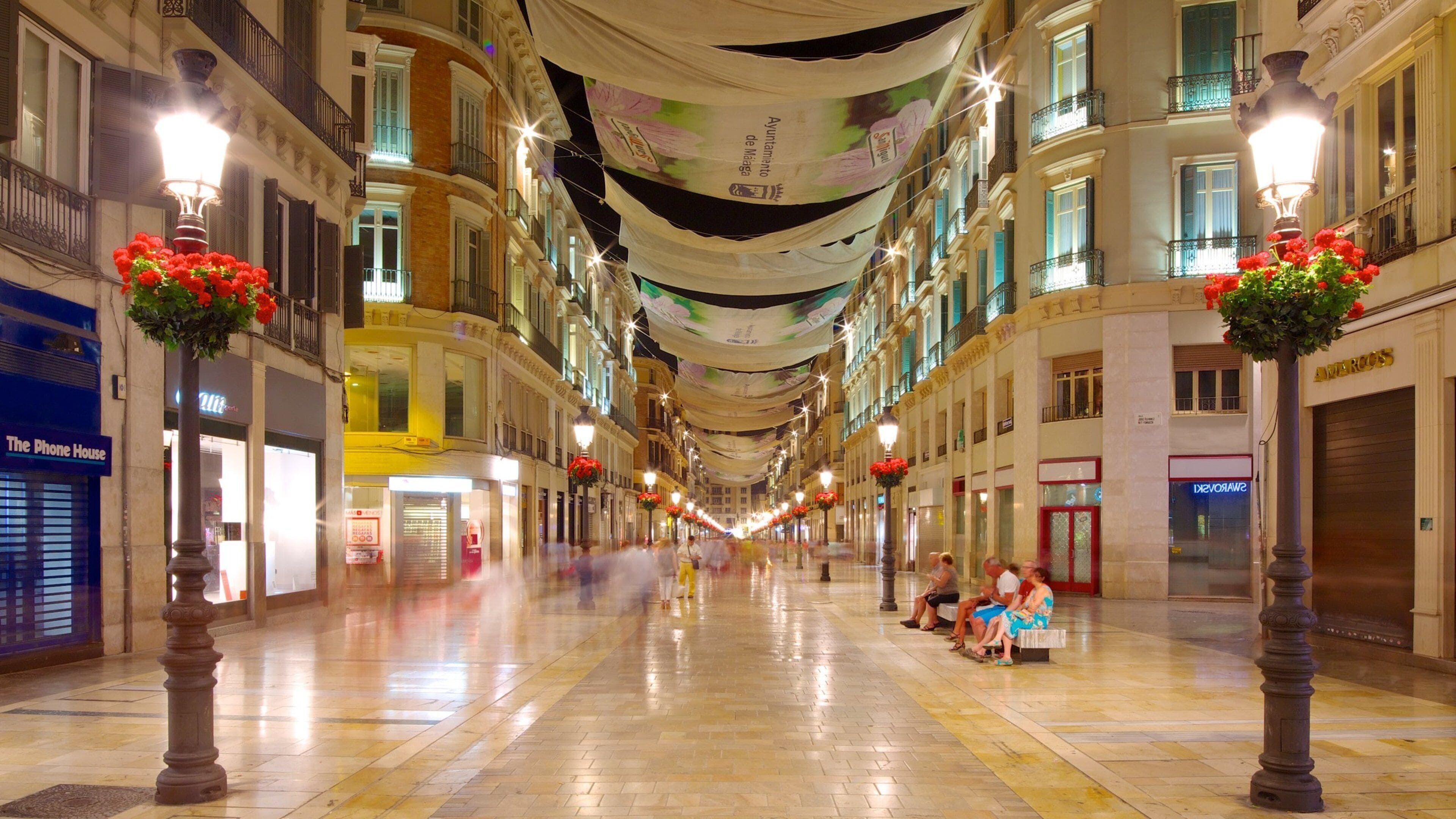 A wide, well-lit pedestrian street with ornate street lamps and hanging banners.
