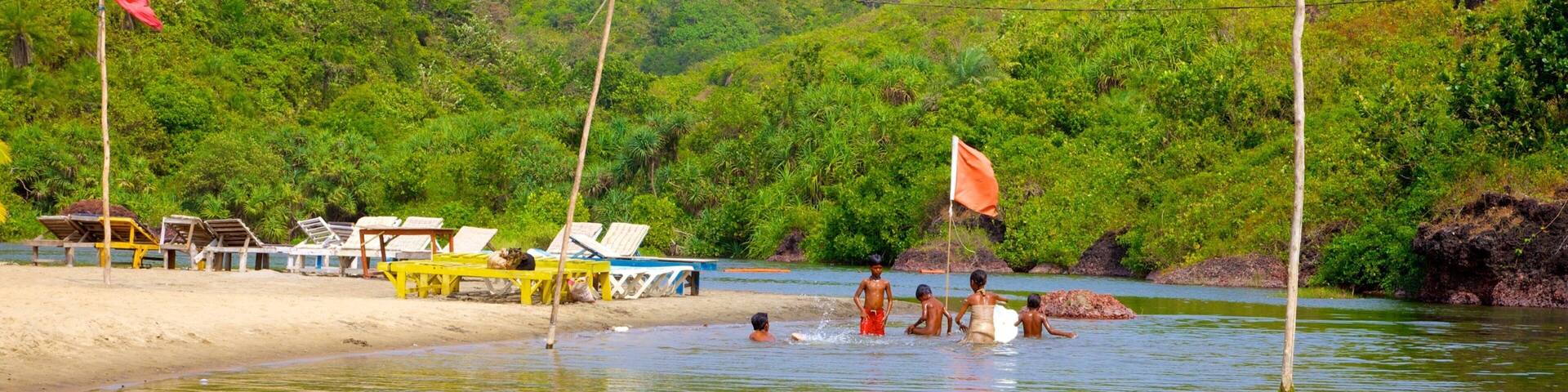 A beach with lounge chairs and flags, surrounded by lush greenery and hills.