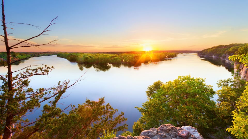 A river surrounded by lush greenery and rocky cliffs during sunset.