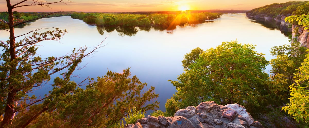 A river surrounded by lush greenery and rocky cliffs during sunset.