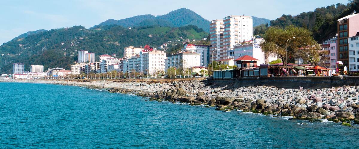 A coastal cityscape with a rocky shoreline, buildings, and a mountain in the background.