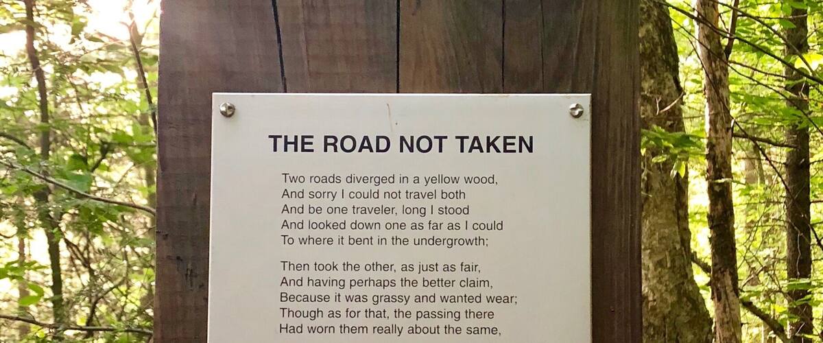 A sign in a forest with a poem titled "The Road Not Taken".