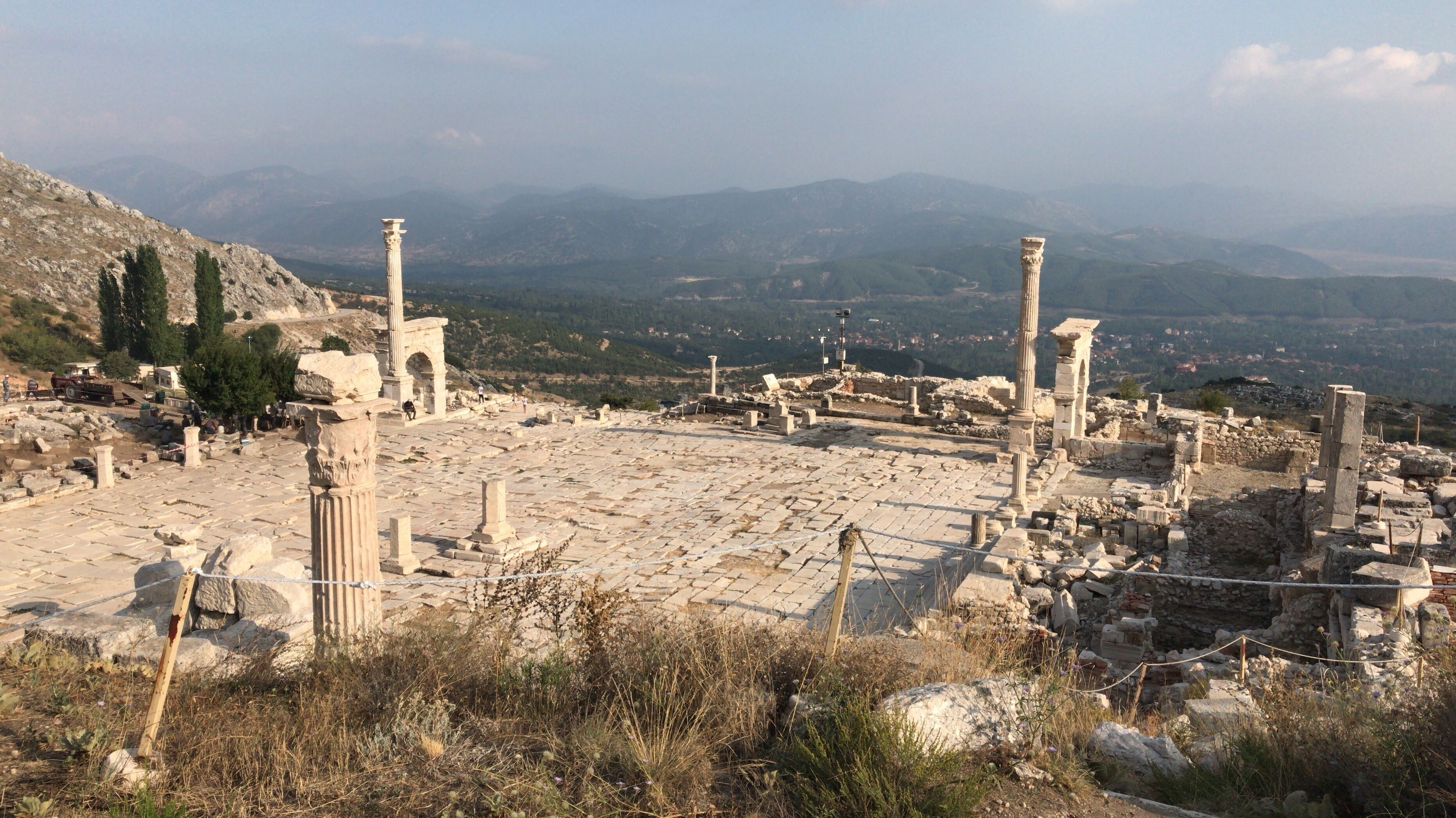 Ancient ruins with columns and stone structures, set against a mountainous backdrop.