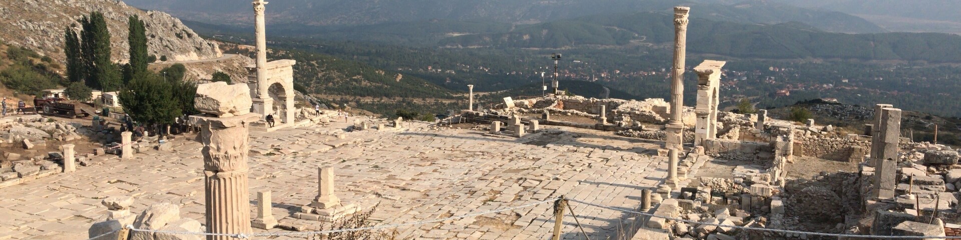 Ancient ruins with columns and stone structures, set against a mountainous backdrop.