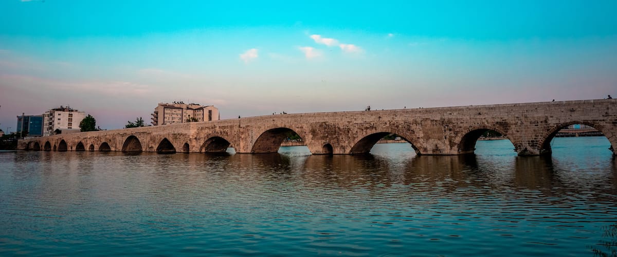 A stone bridge with multiple arches over a body of water, with buildings in the background.