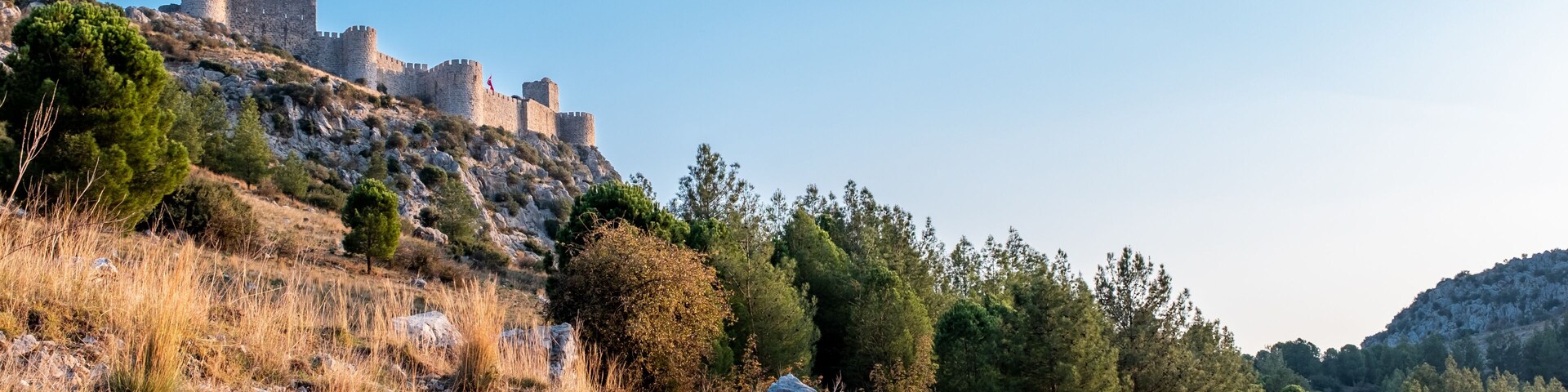 Un camino que lleva a un castillo histórico sobre una colina, rodeado de hierba seca y árboles.