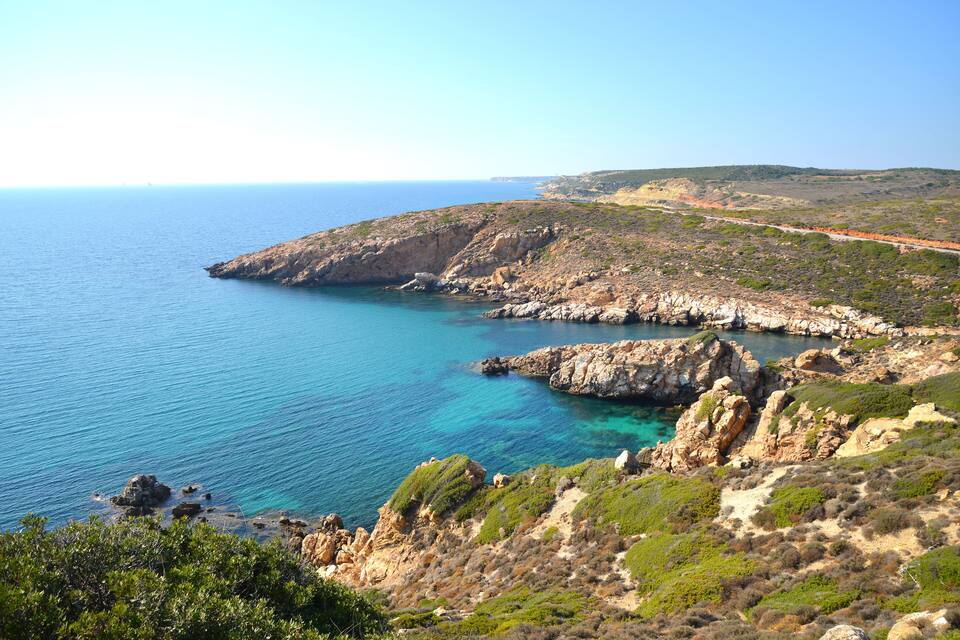 A coastal landscape with rocky terrain and clear blue waters.