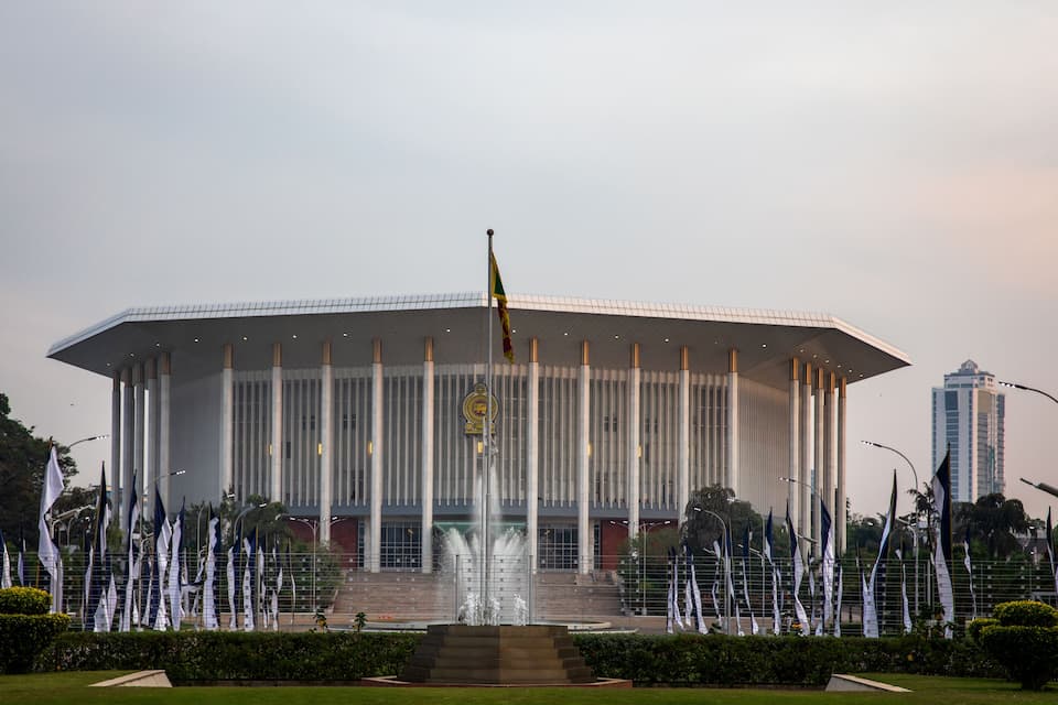 A modern building with a large fountain in front, surrounded by flags.