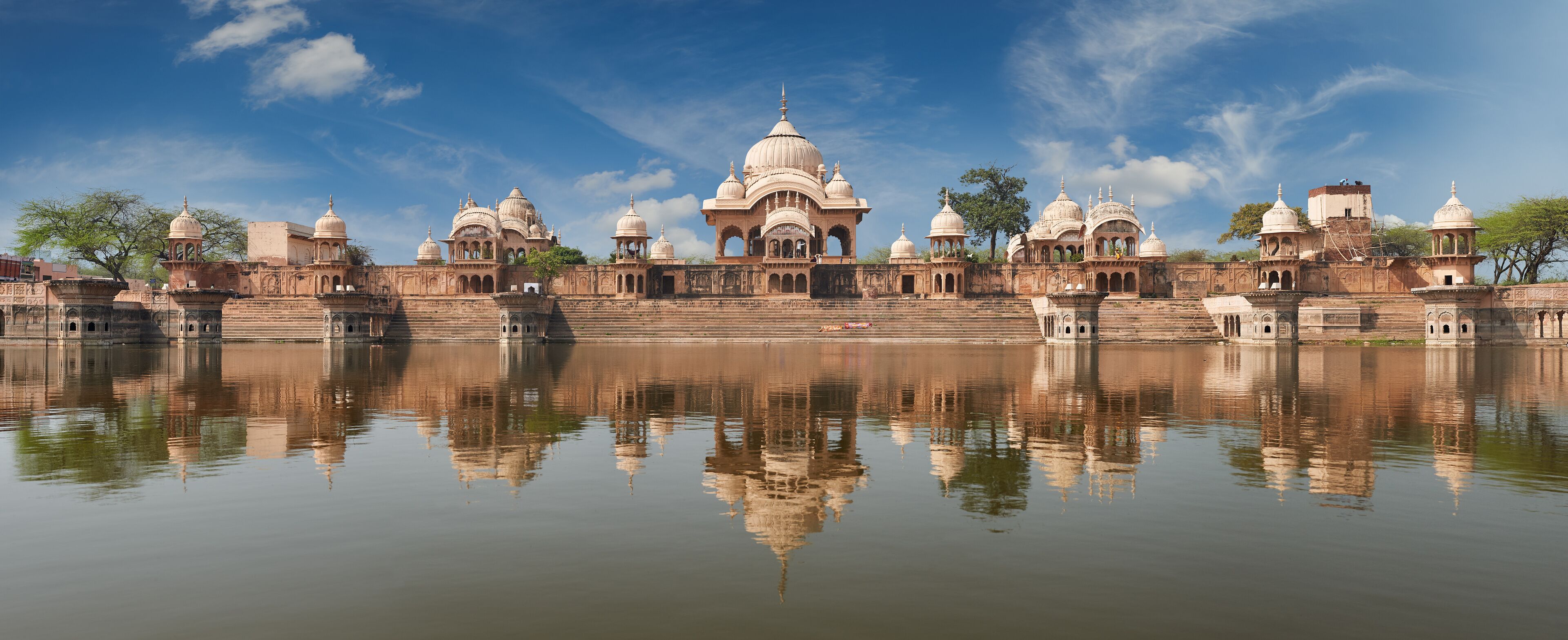 A historic building with multiple domes and arches, reflecting in a calm body of water.
