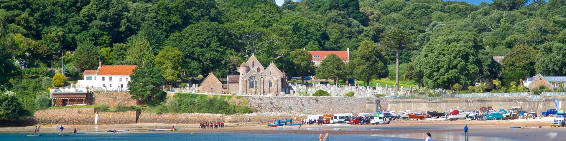 A beach with people, boats, and a church on a hillside.