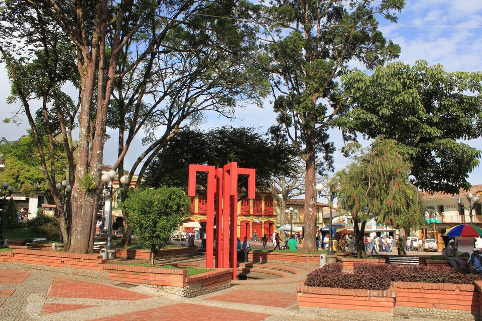 A public square with a red sculpture, trees, and a cobblestone pathway.