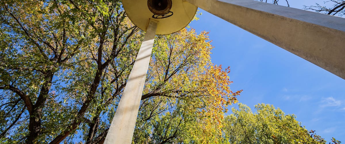 A tall, cylindrical structure with a circular opening at the top, surrounded by trees with green and yellow leaves against a clear blue sky.