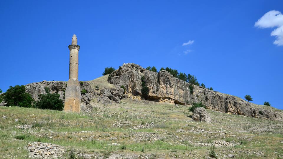 A tall, ancient tower on a rocky hill with sparse vegetation and a clear blue sky.