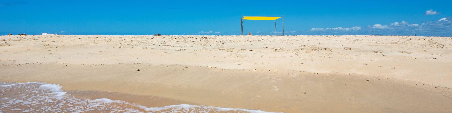 Beautiful beach view from sea point of view and small yellow rustic tent on sunny summer day. Blue sky in the background. Concept of vacations, peace and relaxation. Ponta do Corumbau, Bahia, Brazil.