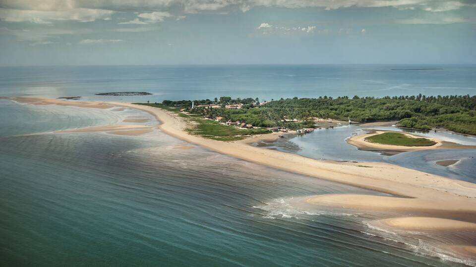 An aerial view of a coastal area with sandy beaches, a river, and a forested hill.