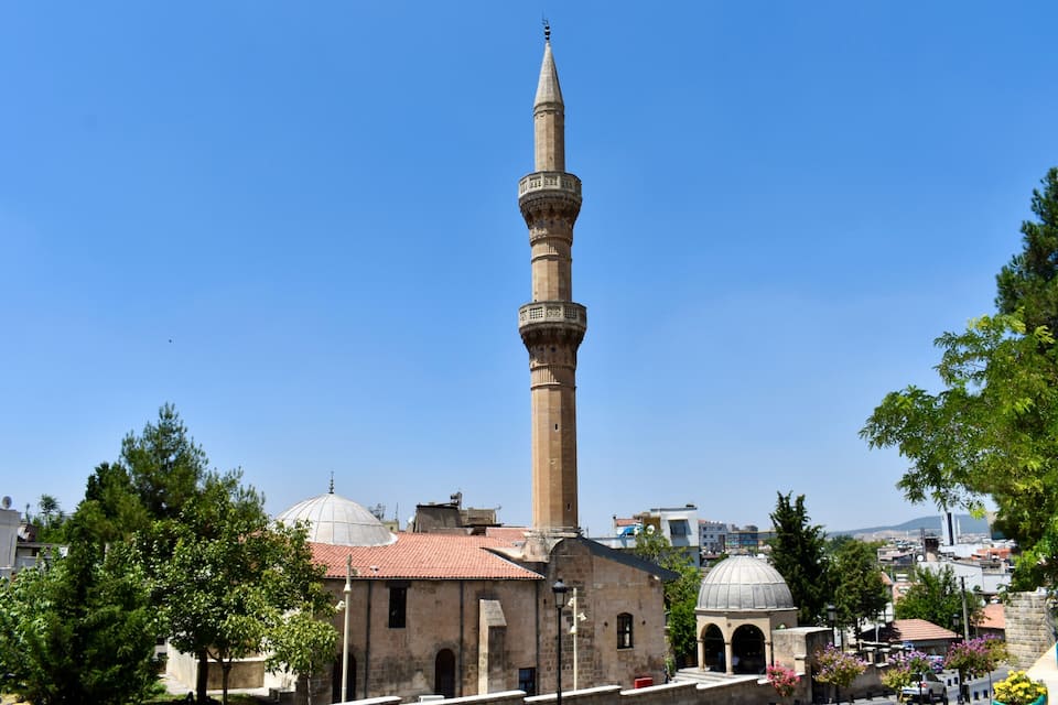A mosque with a tall minaret, domed roof, and a clear blue sky.