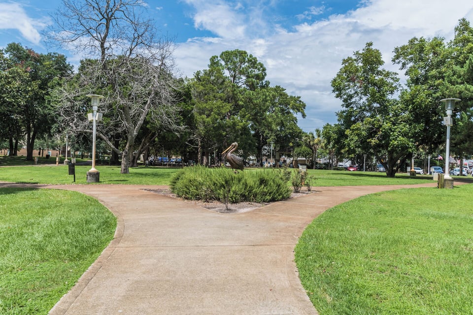 Un parc avec un chemin en béton, de l’herbe verte, des arbres et des lampadaires.