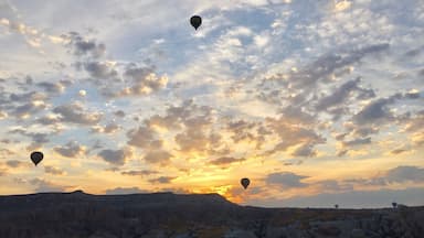A landscape with multiple hot air balloons in the sky during sunset.