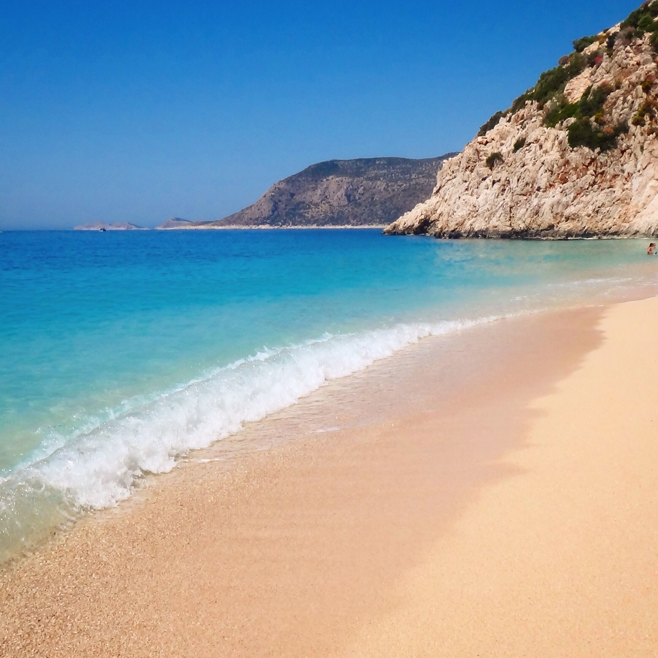 Uma praia arenosa com águas azul-claras e falésias rochosas.