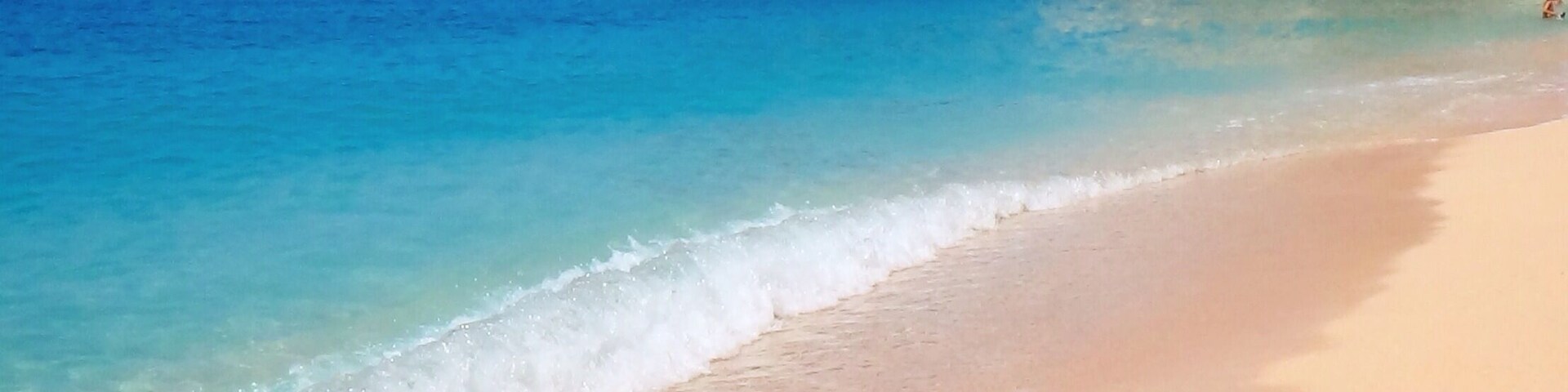 Uma praia arenosa com águas azul-claras e falésias rochosas.