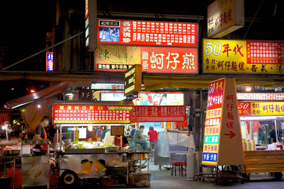 Ein belebter Nachtmarkt mit leuchtenden Schildern in chinesischen Schriftzeichen.