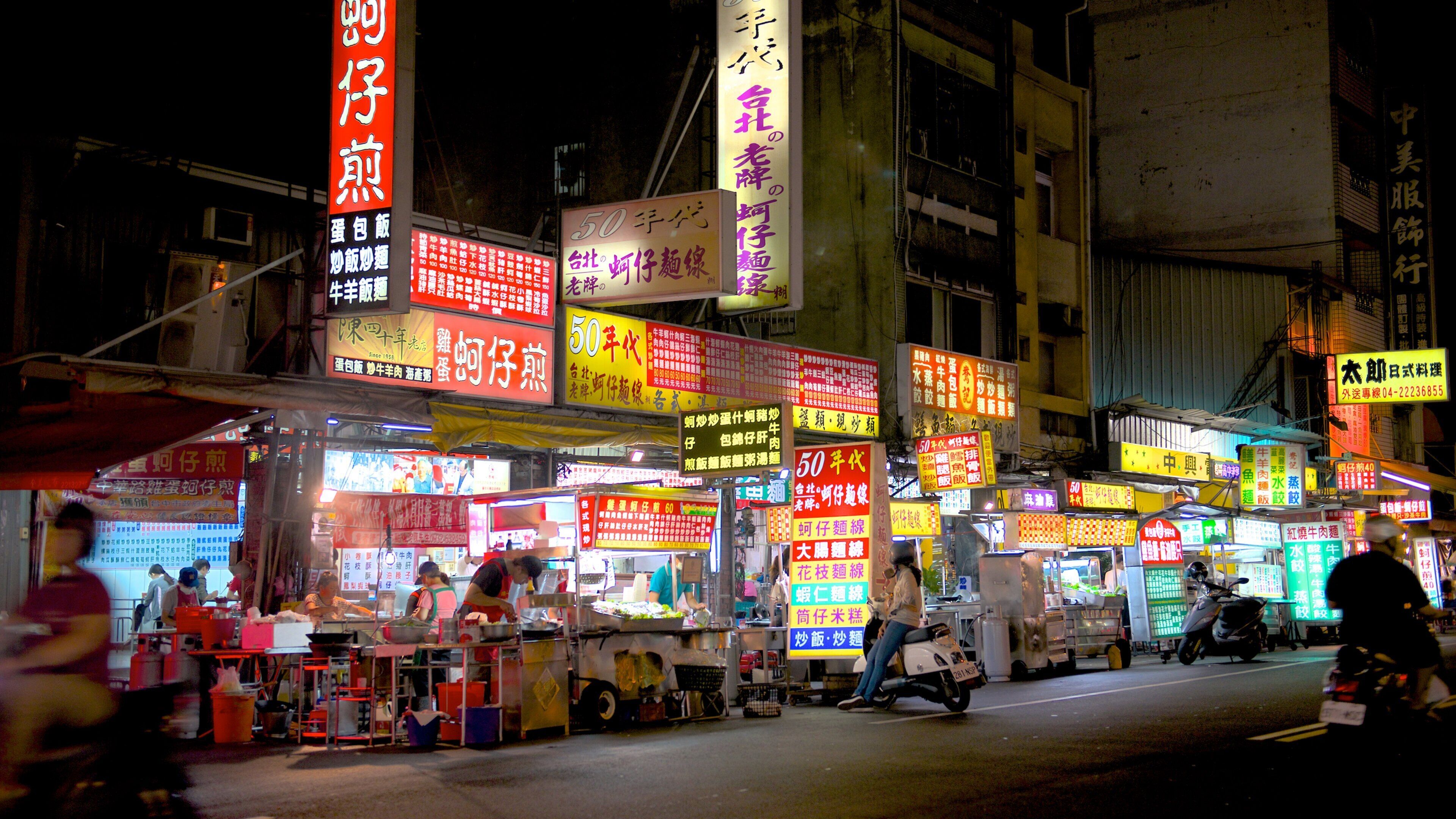 Une rue animée la nuit, avec des enseignes lumineuses et des étals de nourriture.
