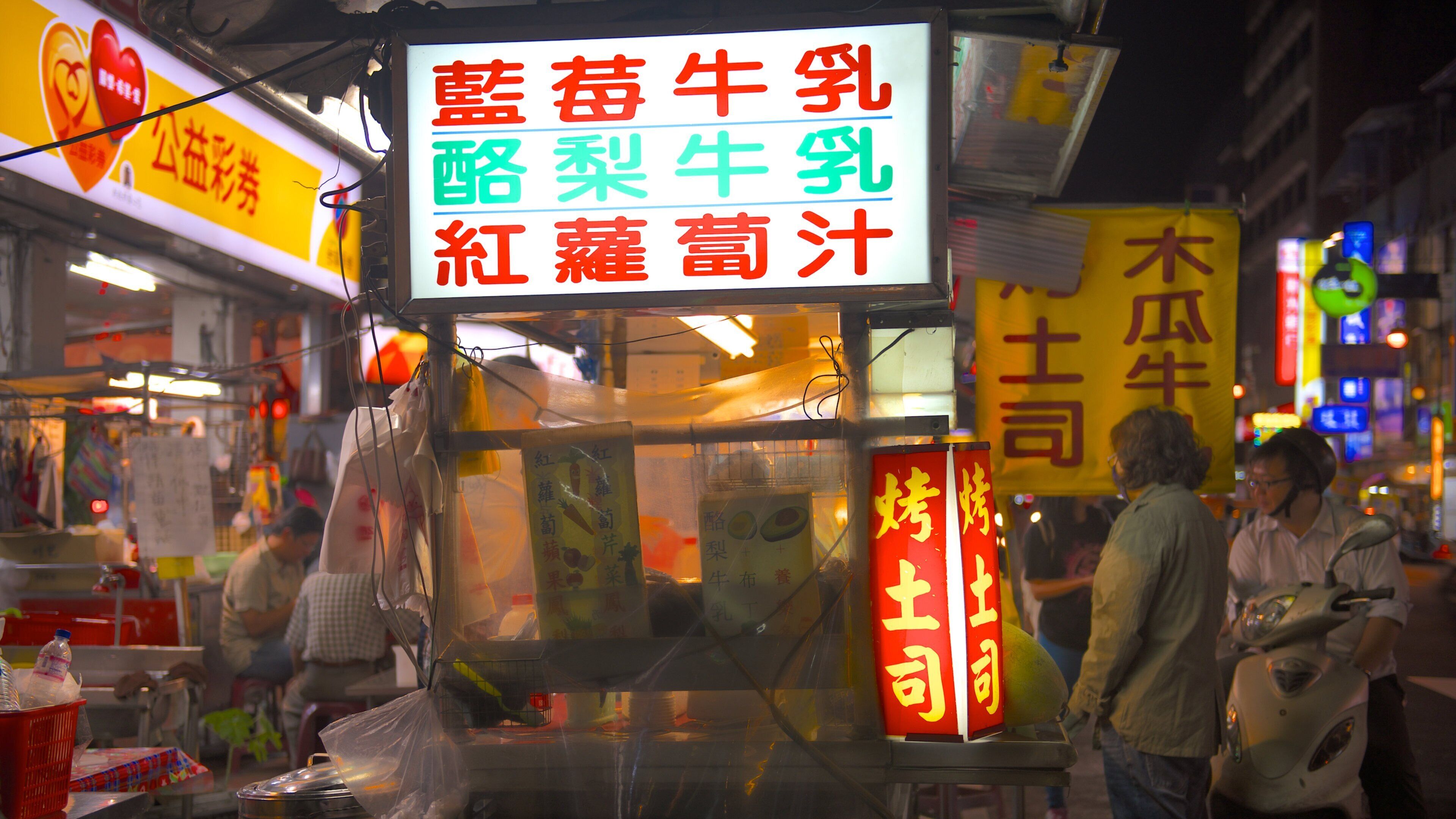 Un stand de nourriture de rue avec une enseigne au néon affichant des caractères chinois.