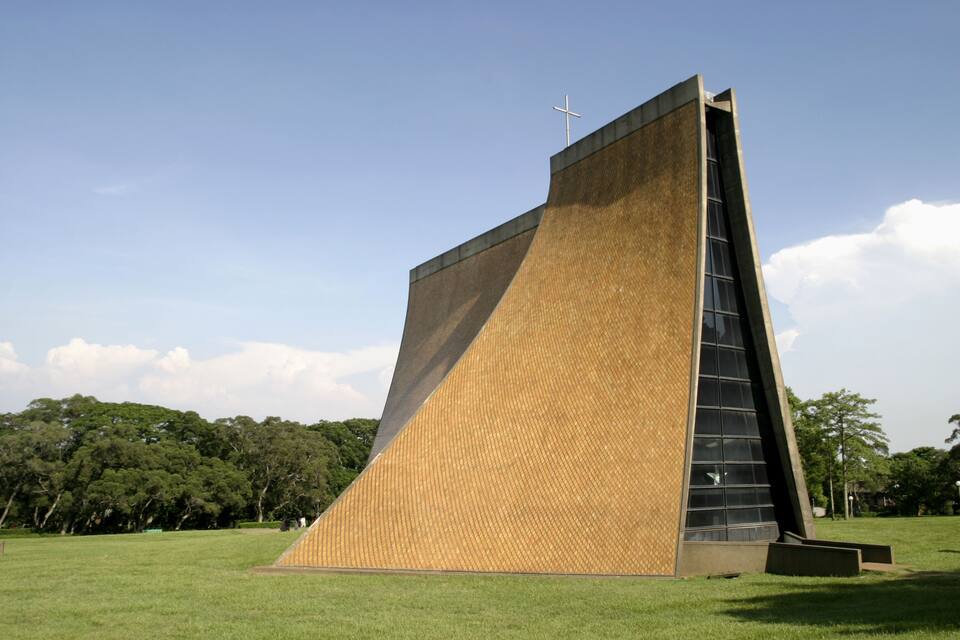 Un edificio moderno con una cruz en la parte superior, rodeado de un campo cubierto de césped y árboles.