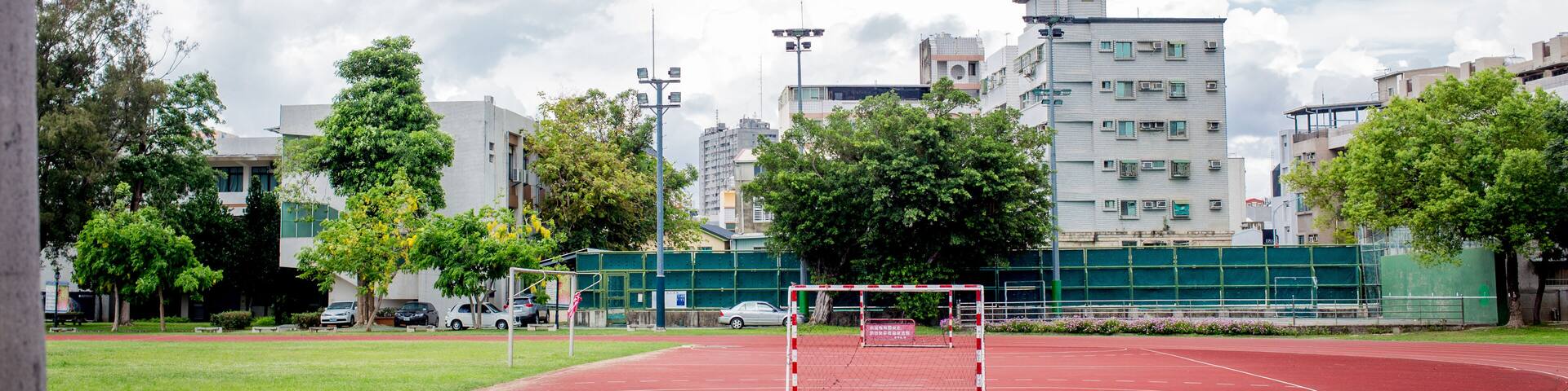 Pista de atletismo roja con un arco de fútbol en el centro, rodeada de árboles y edificios.