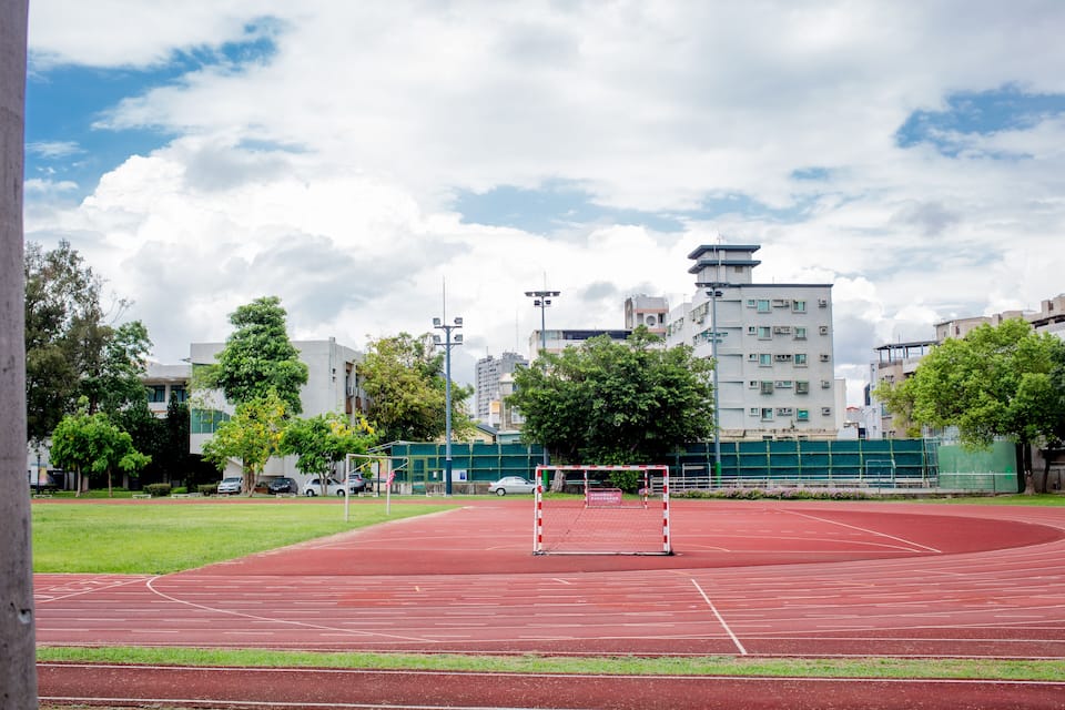 A red running track with a goalpost in the center, surrounded by trees and buildings.