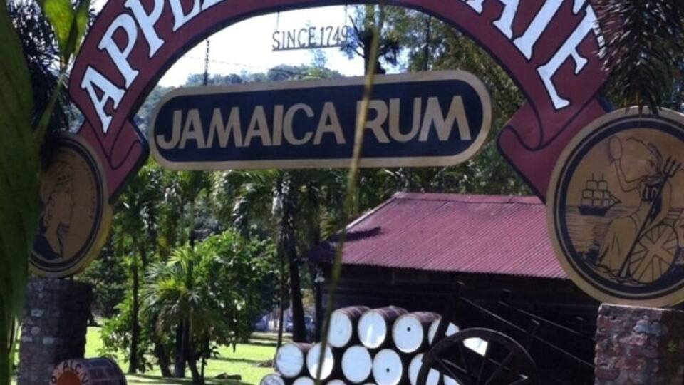 A sign for Appleton Estate, a Jamaican rum brand, with barrels and a cartwheel in the background.
