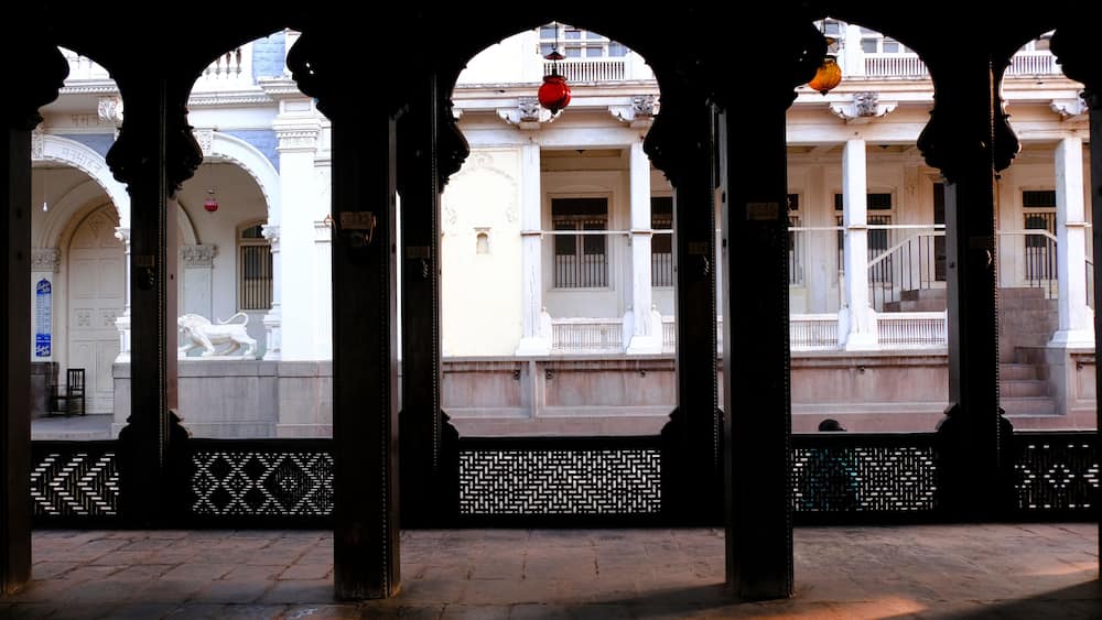 An architectural structure with arches and columns, a lion statue, and a patterned fence.