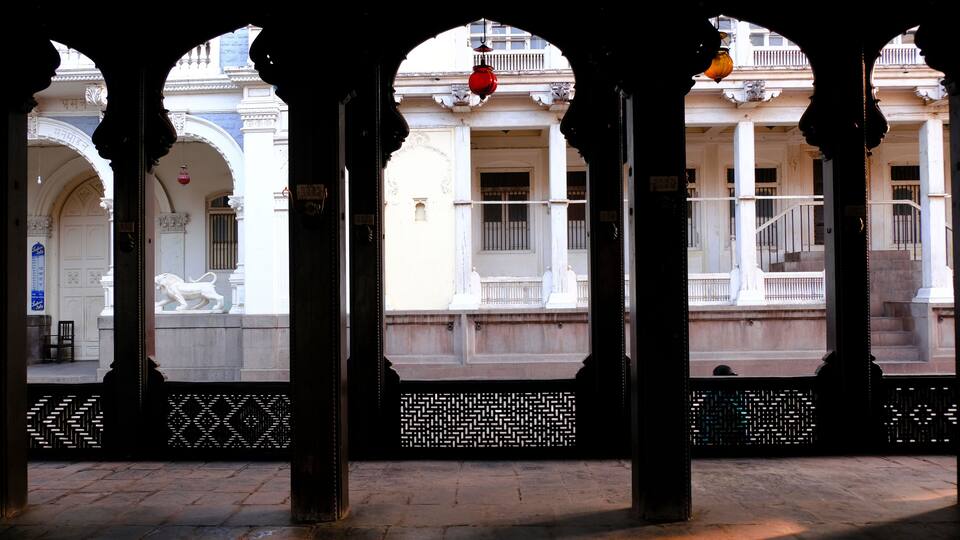An architectural structure with arches and columns, a lion statue, and a patterned fence.