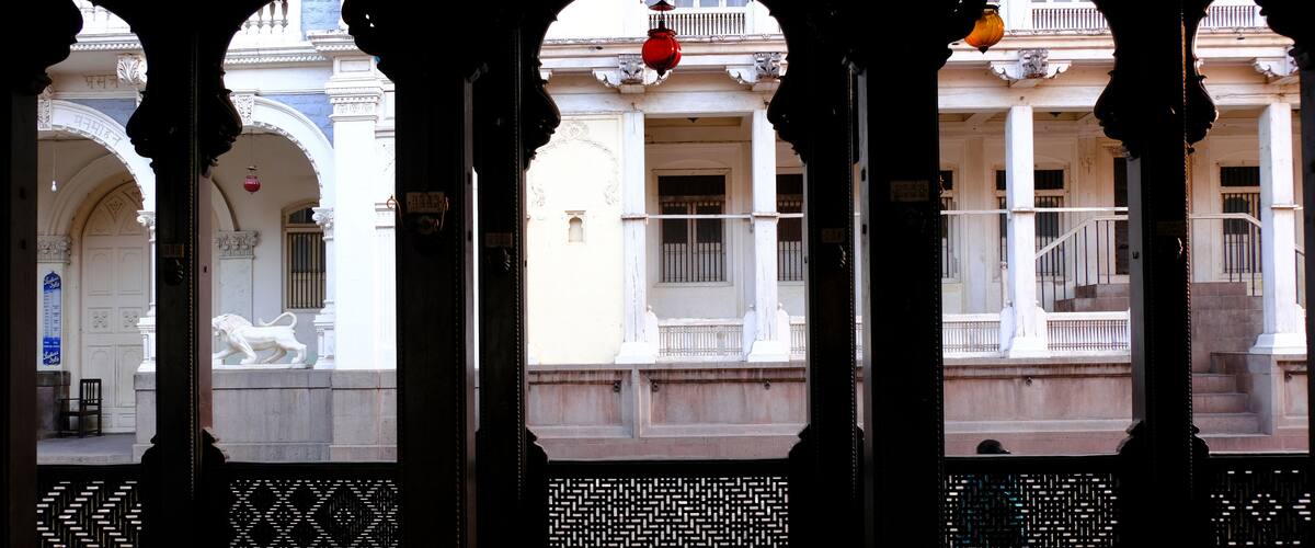 An architectural structure with arches and columns, a lion statue, and a patterned fence.