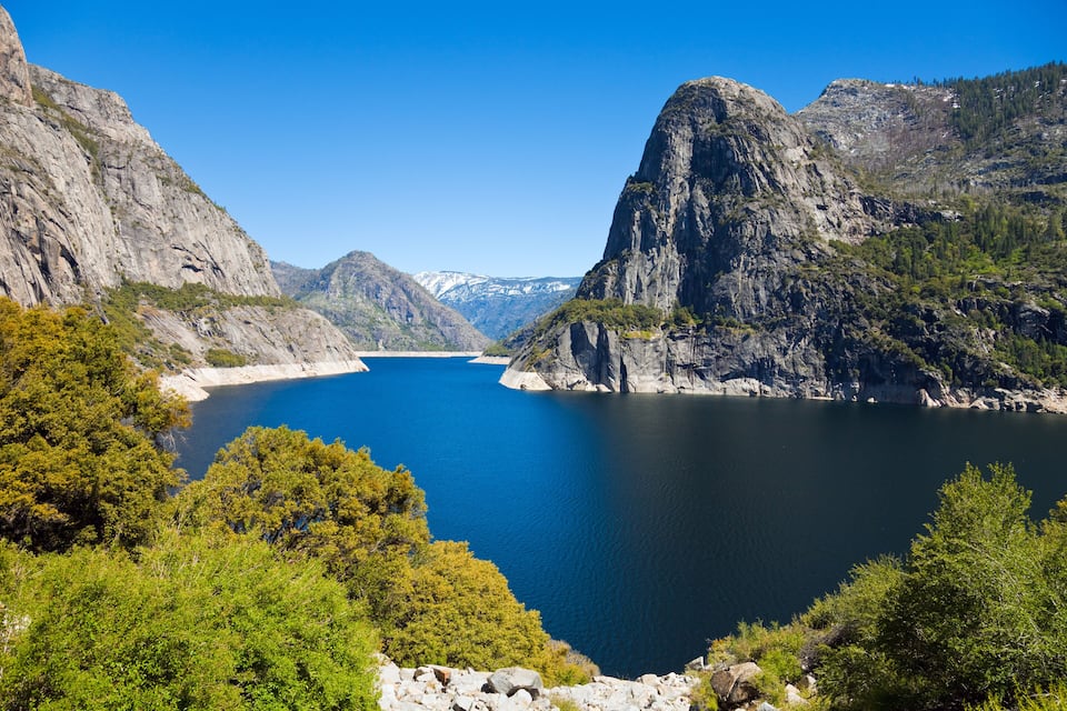 Paisagem montanhosa com um lago azul límpido, rodeado por falésias rochosas e vegetação verde densa.