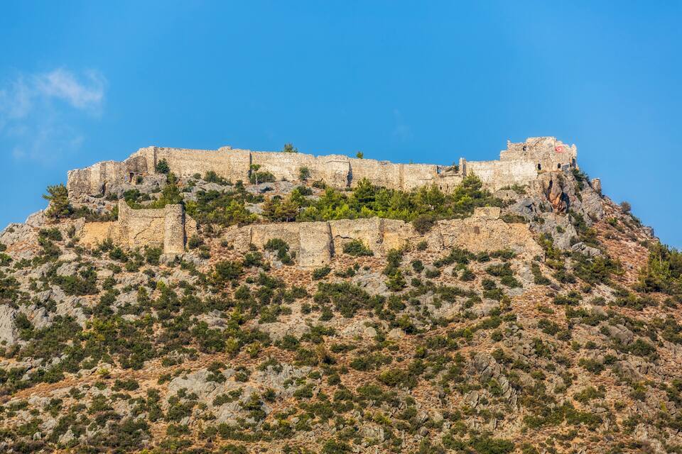 A historic stone fortress on a rocky hill with sparse vegetation.