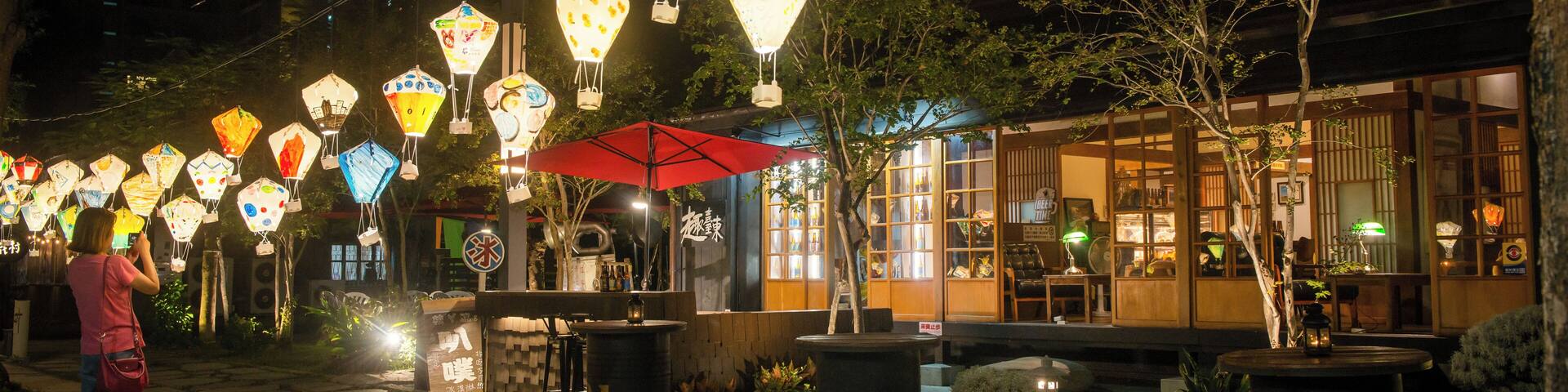 A street at night with lanterns hanging overhead and a person taking a photo.