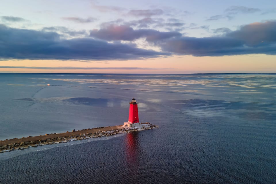 A red lighthouse on a rocky outcrop in the ocean.